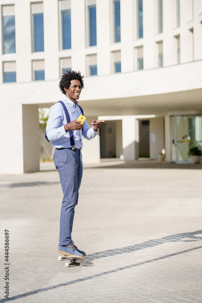 Fototapeta premium Black businessman on a skateboard holding a smartphone outdoors.