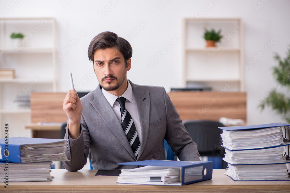 Young male employee unhappy with excessive work in the office Young male employee unhappy with excessive work in the office