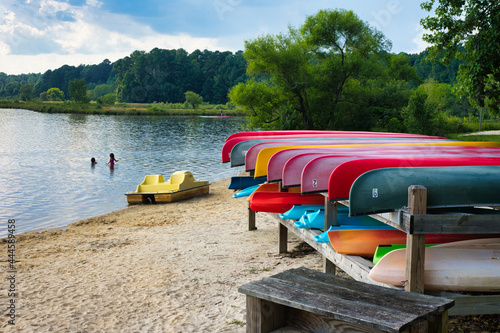 Fototapeta A summer lakeside beach landscape with colorful canoe racks.