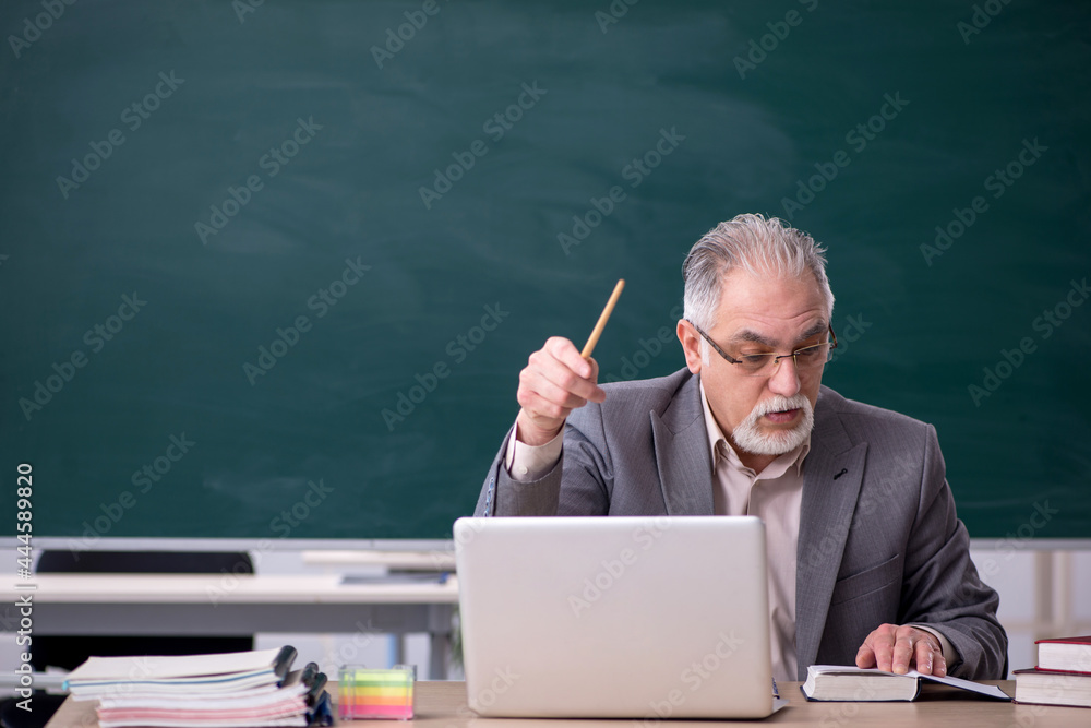 Old male teacher in front of blackboard Old male teacher in front of blackboard