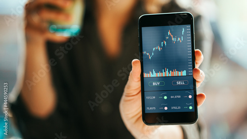 Fototapeta Naklejka Na Ścianę i Meble -  Woman using mobile phone investing application. Stock market investment app in hand. Screen showing close-up