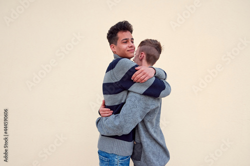 A young interracial gay couple hugging isolated on a beige background