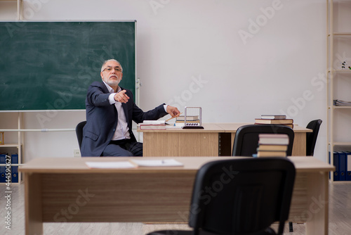 Old male teacher in front of blackboard