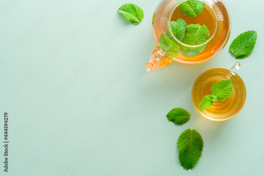 Cup and teapot with mint tea and leaves on green background. Herbal tea concept. Flat lay, top view, copy space Cup and teapot with mint tea and leaves on green background. Herbal tea concept. Flat lay, top view, copy space