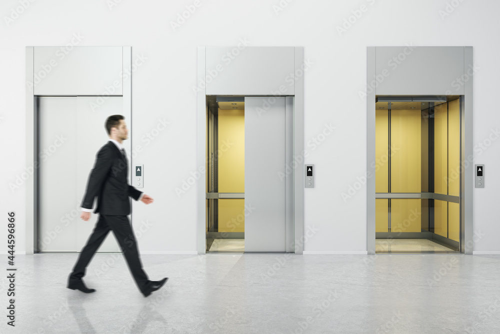 Fototapeta premium Businessman walking in white concrete interior with three elevator doors. Opportunity and success concept.