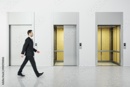 Businessman walking in white concrete interior with three elevator doors. Opportunity and success concept.