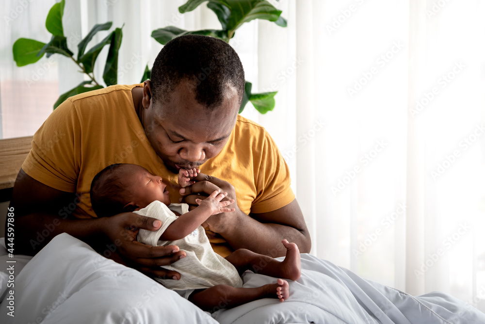 An African American father kissing hand, his 12-day-old baby black skin newborn son lying in bed, with happy, concept to African American family and newborn An African American father kissing hand, his 12-day-old baby black skin newborn son lying in bed, with happy, concept to African American family and newborn