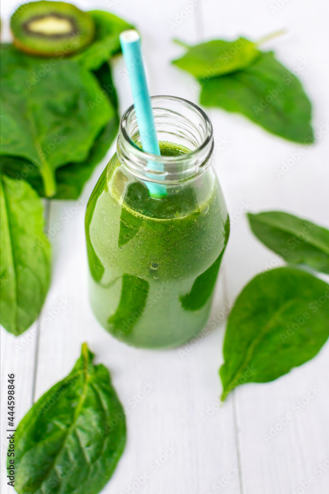 Healthy detox green smoothie with kiwi and spinach leaves in a glass bottle with a straw on a white wooden background. Healthy lifestyle concept. Healthy detox green smoothie with kiwi and spinach leaves in a glass bottle with a straw on a white wooden background. Healthy lifestyle concept.