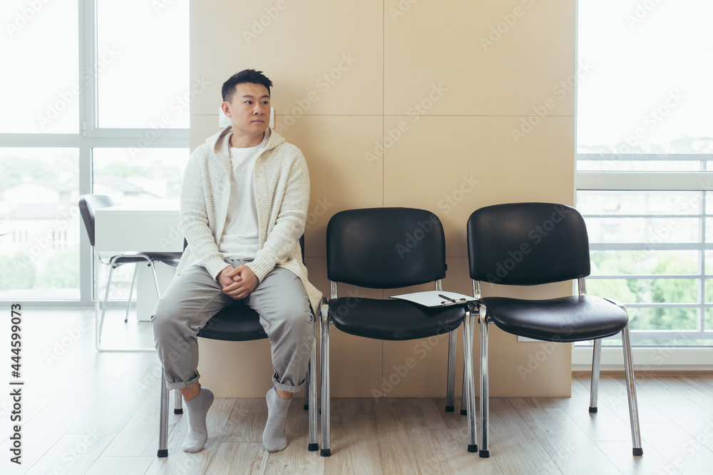 young asian man waiting for an interview or meeting sitting in the hallway in the waiting room. Student or entrant in the reception for exam or employment hr. Male patient in office a hospital clinic young asian man waiting for an interview or meeting sitting in the hallway in the waiting room. Student or entrant in the reception for exam or employment hr. Male patient in office a hospital clinic