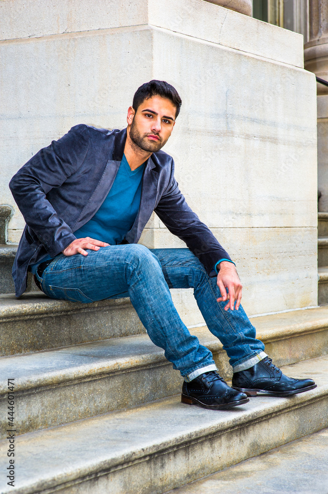 Dressing in a dark purple woolen blazer, blue jeans and black leather shoes, a young Middle Eastern guy with bread and mustache is sitting on steps, thoughtfully looking at you.. Dressing in a dark purple woolen blazer, blue jeans and black leather shoes, a young Middle Eastern guy with bread and mustache is sitting on steps, thoughtfully looking at you..