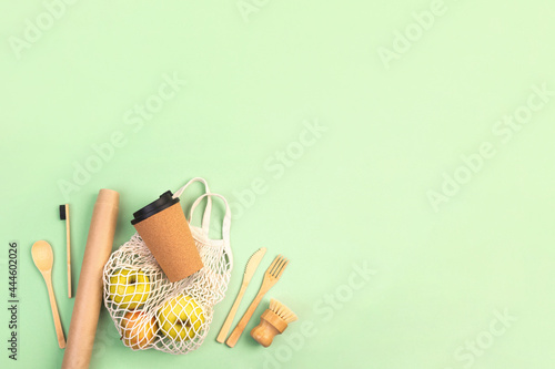 Reusable wooden cutlery, cork mug and grocery bag with apples. Dishwashing brush and kraft wrapping paper, eco friendly fork, knife, spoon on green backdrop. Zero waste concept. Copyspace, flatlay.