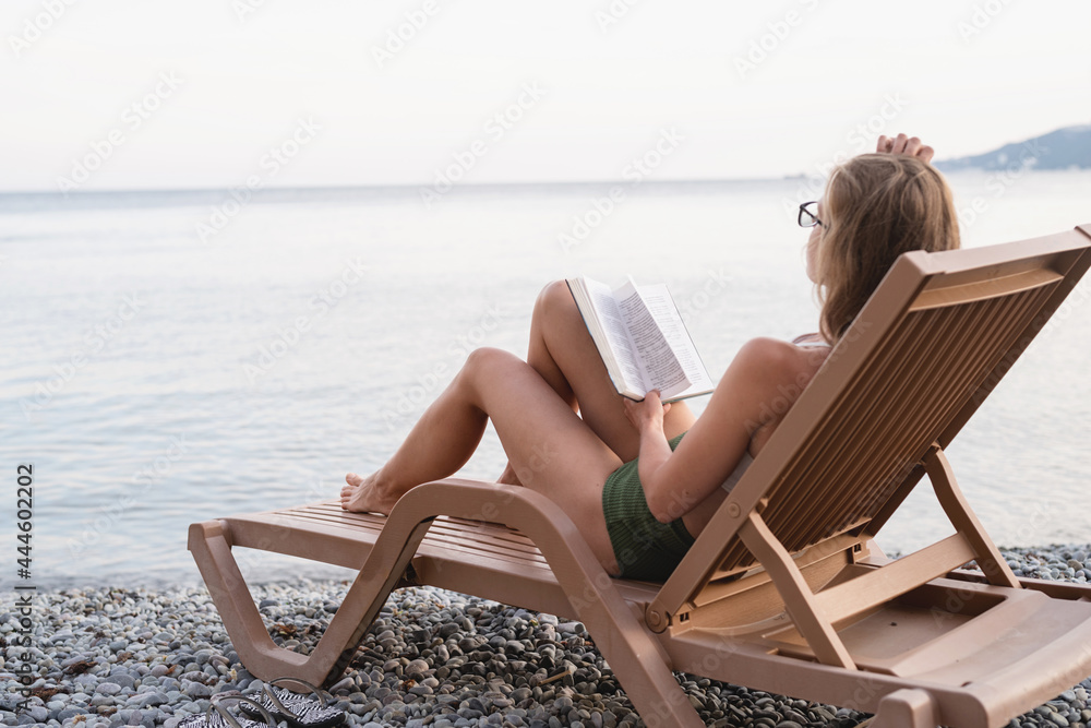 The beautiful young woman lying on the sun lounger reading a book