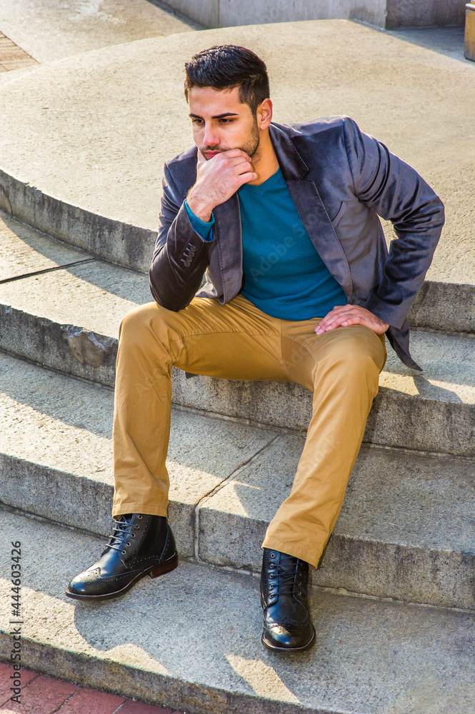 Dressing in a dark purple woolen blazer,  dark yellow pants and leather boot shoes, a young Middle East guy with bread and mustache is sitting on circle steps, relaxing and thinking.