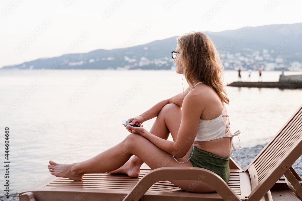 The beautiful young woman sitting on the sun lounger listening to the music