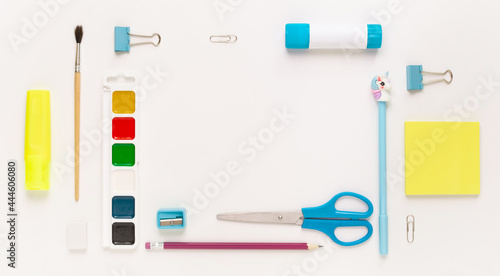 Top view of modern white, blue, yellow office desktop with school supplies and stationery on table around empty space for text. Back to school concept flat lay with mockup