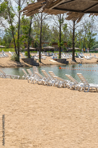 A lot of free white plastic sun beds on the sand near the lake. Sun loungers on the beach