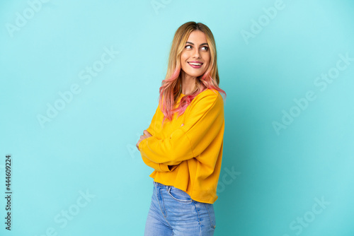 Young woman over isolated blue background looking to the side and smiling