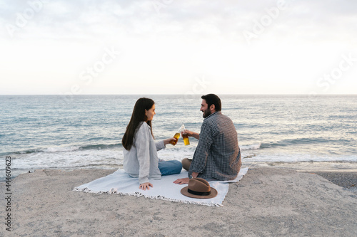 Couple enjoying seaside view, drinking beer alone. Portrait of happy people spending time picnic leisure together on the sunset.