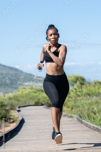 Vigorous afro american woman running along a wooden runway: Exercise and lifestyle concept.