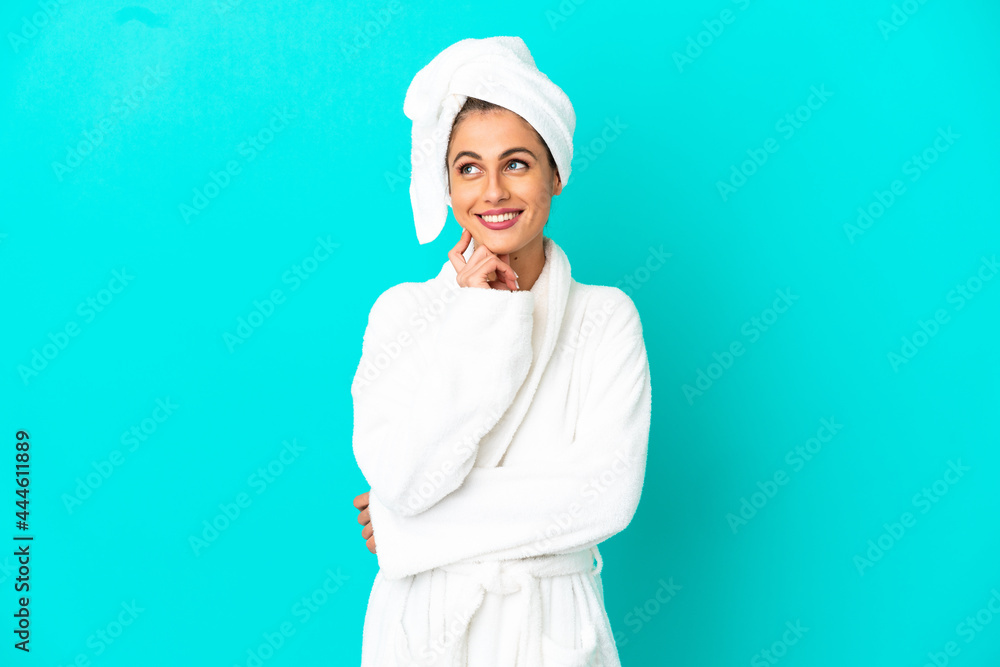 Young woman in a bathrobe over isolated blue background thinking an idea while looking up Young woman in a bathrobe over isolated blue background thinking an idea while looking up