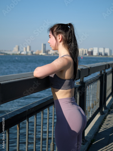 A girl with an athletic figure in a light lilac sports uniform stands on the Kremlin embankment in Kazan. Leaned against the railing. Look at the water. © Aleksandr