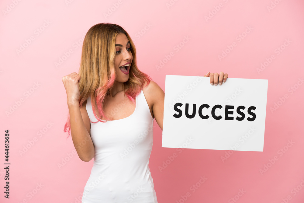 Young woman over isolated pink background holding a placard with text SUCCESS and celebrating a victory Young woman over isolated pink background holding a placard with text SUCCESS and celebrating a victory