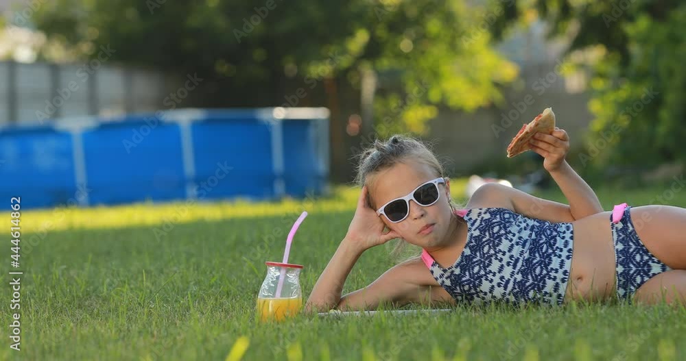 Teen Girl In A Swimsuit And Sunglasses Is Eating Pizza At Green Lawn teen-girl-in-a-swimsuit-and-sunglasses-is-eating-pizza-at-green-lawn