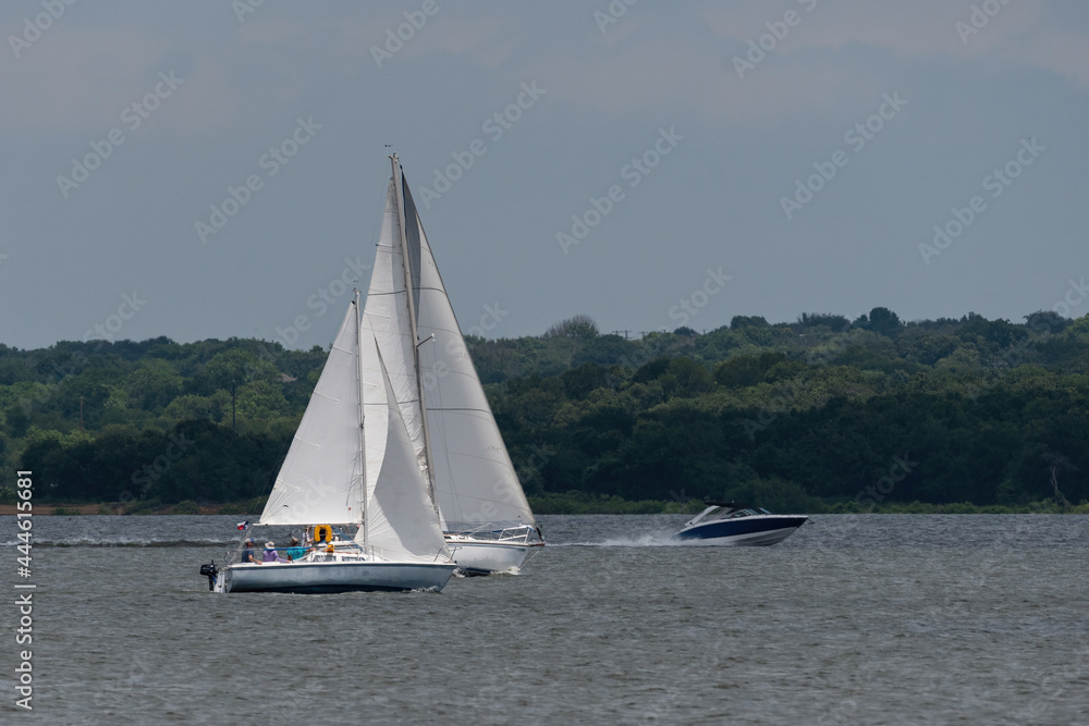 Sailboats sailing on a lake while a powerboat passes behind