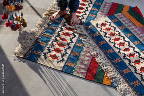 hand woven and knotted Persian kilim on the floor and a man standing on it with colorful tassels 
