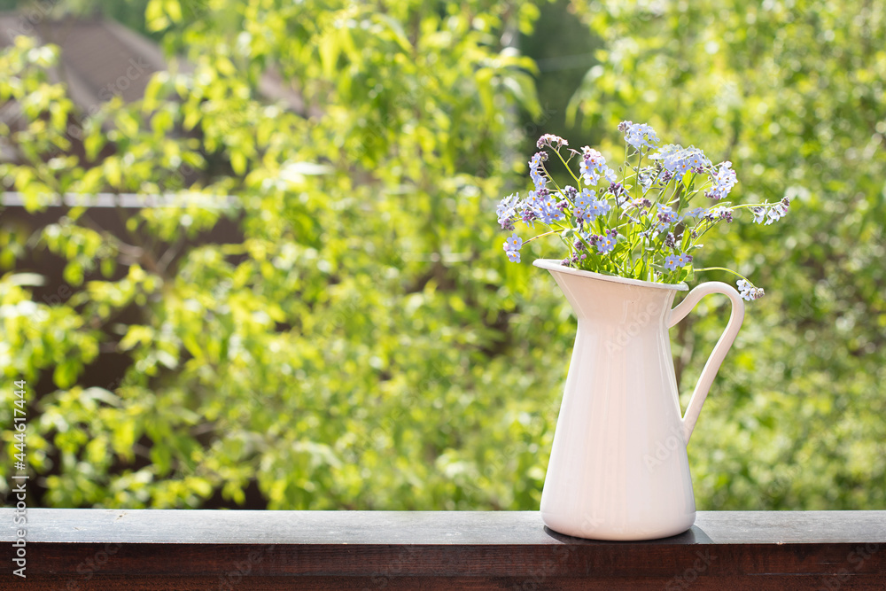 Delicate forget-me-not flowers in a white jug on a green summer background. Copy space Delicate forget-me-not flowers in a white jug on a green summer background. Copy space