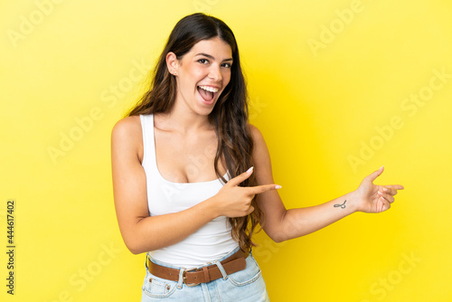 Young caucasian woman isolated on yellow background surprised and pointing side