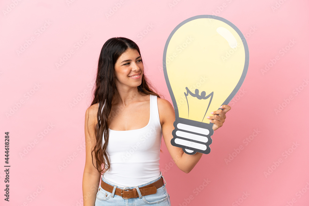 Young caucasian woman isolated on pink background holding a bulb icon with happy expression Young caucasian woman isolated on pink background holding a bulb icon with happy expression