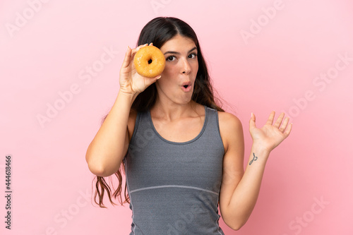Young caucasian woman isolated on pink background holding a donut in an eye
