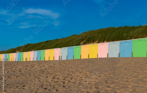 Colorful beach huts on a sunny summer day with blue sky. Tourists like the tiny houses with the colored doors. Typical storage rooms for beach equipment in the netherlands. 