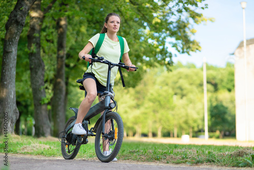 beautiful girl traveling on electric bike, active young woman riding bicycle, female biking in park, in nature at summer. travel, healthy lifestyle, sport concept