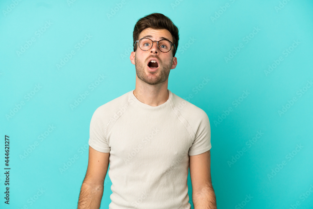 Young caucasian handsome man isolated on blue background looking up and with surprised expression Young caucasian handsome man isolated on blue background looking up and with surprised expression