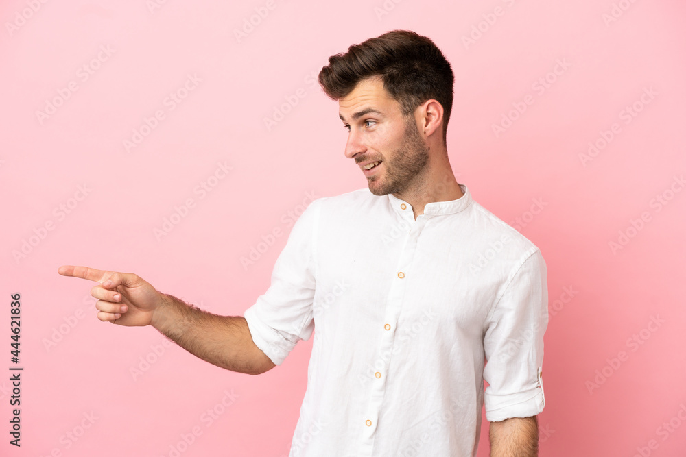 Young caucasian handsome man isolated on pink background pointing finger to the side and presenting a product