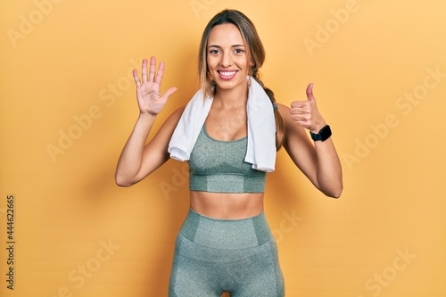 Beautiful hispanic woman wearing sportswear and towel showing and pointing up with fingers number six while smiling confident and happy.