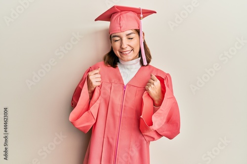 Young caucasian woman wearing graduation cap and ceremony robe excited for success with arms raised and eyes closed celebrating victory smiling. winner concept.