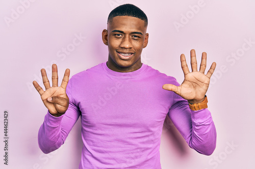 Young black man wearing casual pink sweater showing and pointing up with fingers number nine while smiling confident and happy.