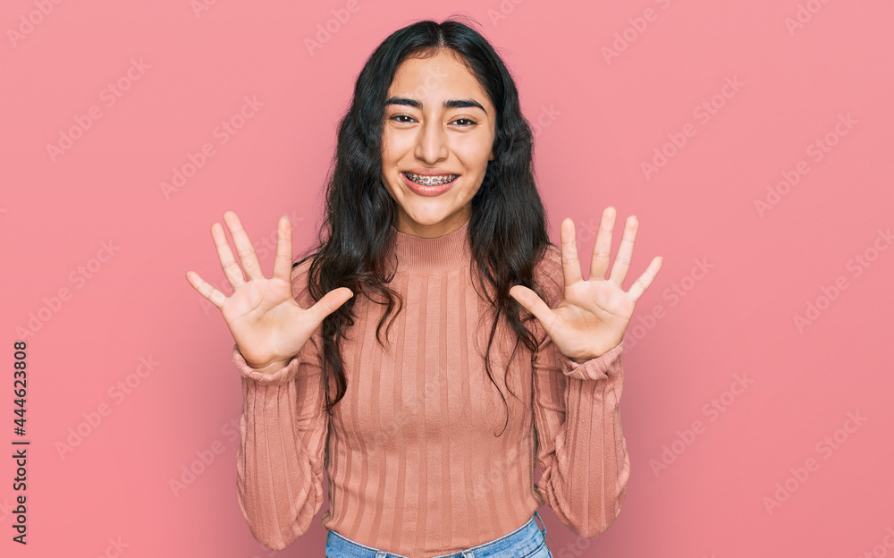 Hispanic teenager girl with dental braces wearing casual clothes showing and pointing up with fingers number ten while smiling confident and happy. Hispanic teenager girl with dental braces wearing casual clothes showing and pointing up with fingers number ten while smiling confident and happy.