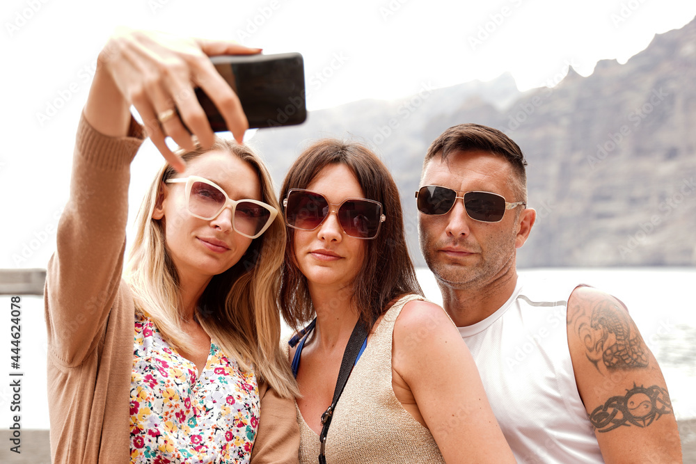 Three smiling friends taking selfie photos at digital camera of smartphone. Summer time. Three smiling friends taking selfie photos at digital camera of smartphone. Summer time.