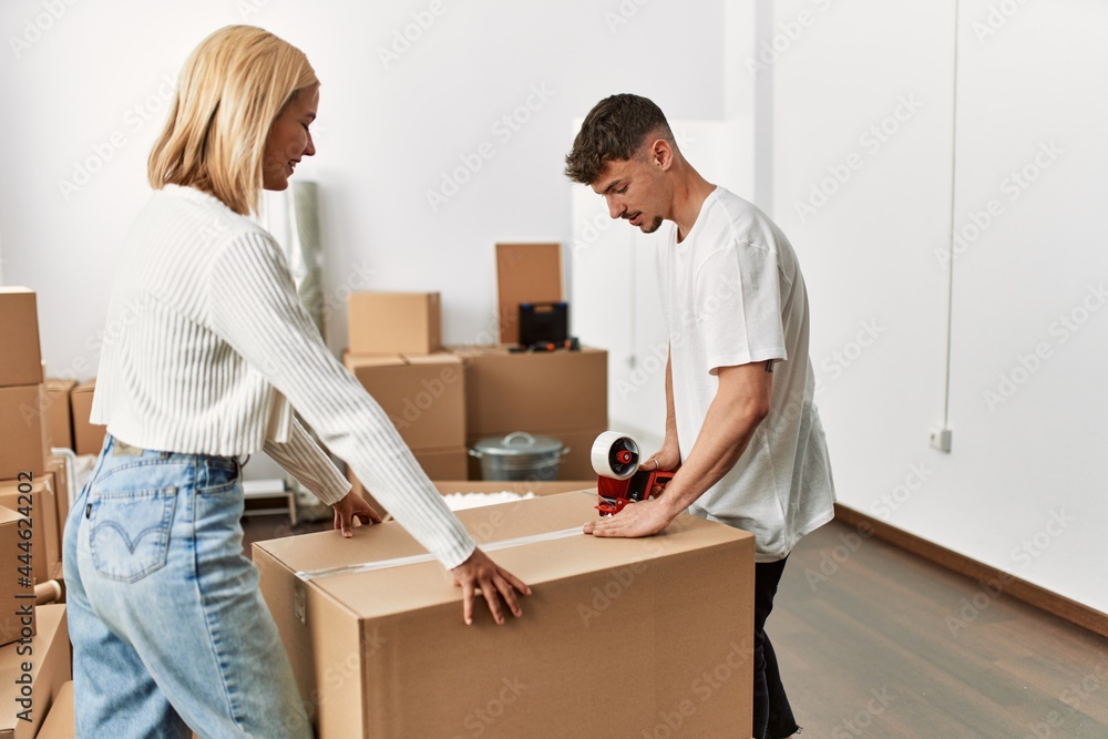 Young caucasian couple smiling happy closing box using packing tape at new home. Young caucasian couple smiling happy closing box using packing tape at new home.