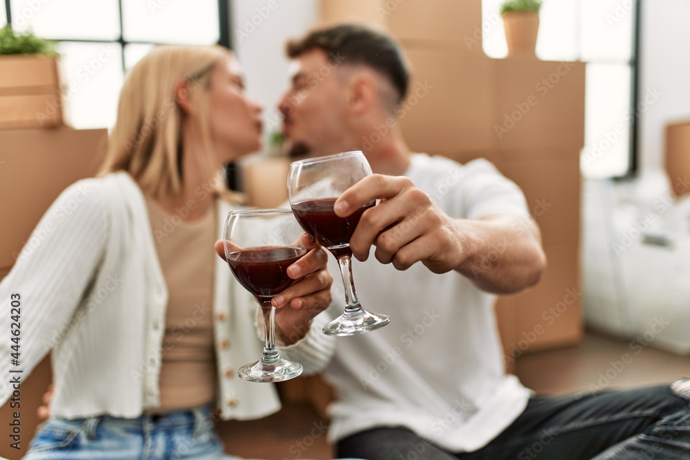 Young caucasian couple toasting with red wine glass sitting at new home. Young caucasian couple toasting with red wine glass sitting at new home.