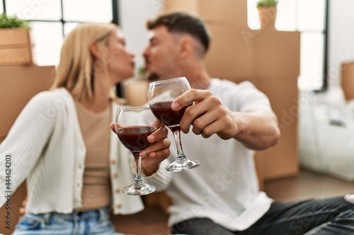 Young caucasian couple toasting with red wine glass sitting at new home.