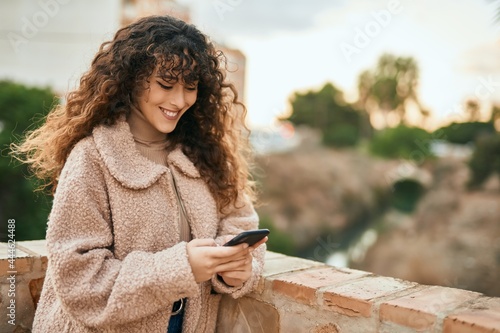 Young hispanic woman smiling happy using smartphone at the city