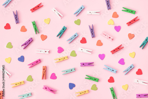 Small colorful wooden laundry tongs with colorful wooden hearts arranged on a pink background..