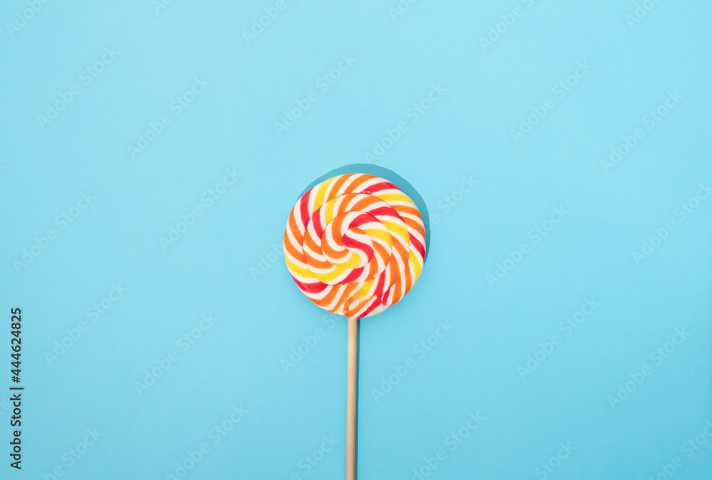 Colorful round lollipop with wooden handle on a blue background. Colorful round lollipop with wooden handle on a blue background.