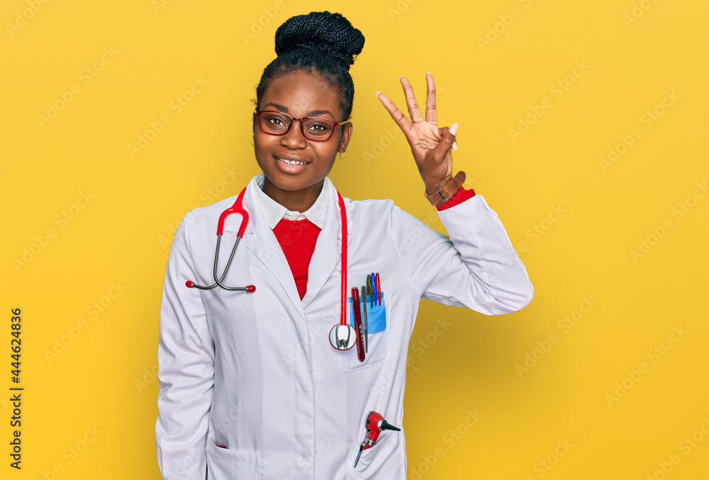 Young african american woman wearing doctor uniform and stethoscope showing and pointing up with fingers number three while smiling confident and happy. Young african american woman wearing doctor uniform and stethoscope showing and pointing up with fingers number three while smiling confident and happy.