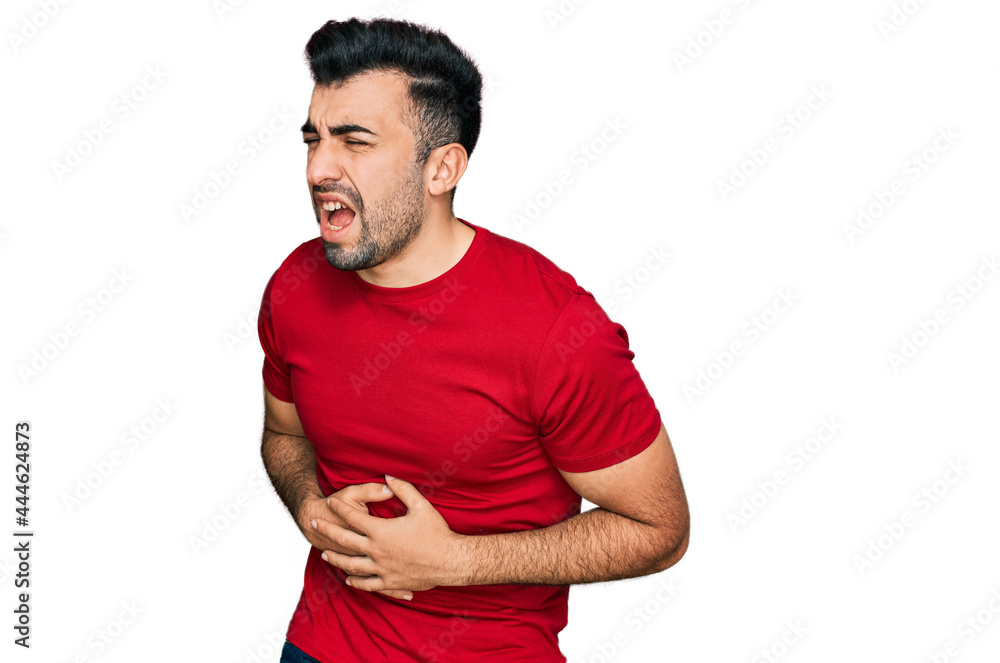Hispanic man with beard wearing casual red t shirt with hand on stomach because nausea, painful disease feeling unwell. ache concept. Hispanic man with beard wearing casual red t shirt with hand on stomach because nausea, painful disease feeling unwell. ache concept.